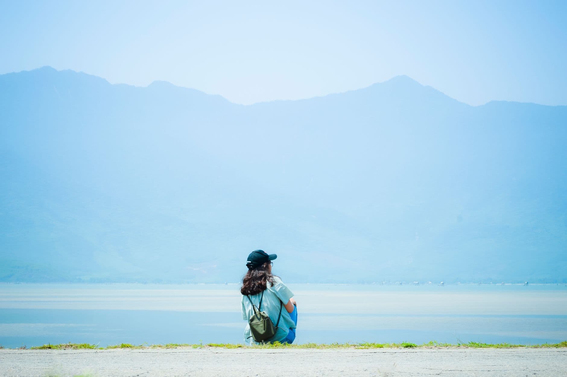 A person sitting quietly by a calm lake, looking out at misty hills